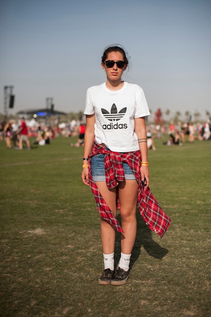 A woman in a white Adidas T-shirt with the old school logo, blue denim shorts, and a red checked shi...