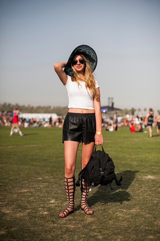 A woman in a white top, black leather shorts, black knee-high roman sandals, a black hat, and backpa...