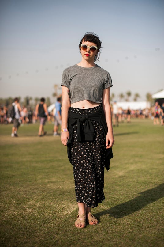 A woman in a grey shirt and long black skirt with a white floral pattern, a sweater tied around her ...