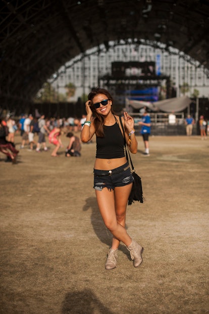 A woman in a crop tank top, black hot pants, and beige leather boots and black sunglasses