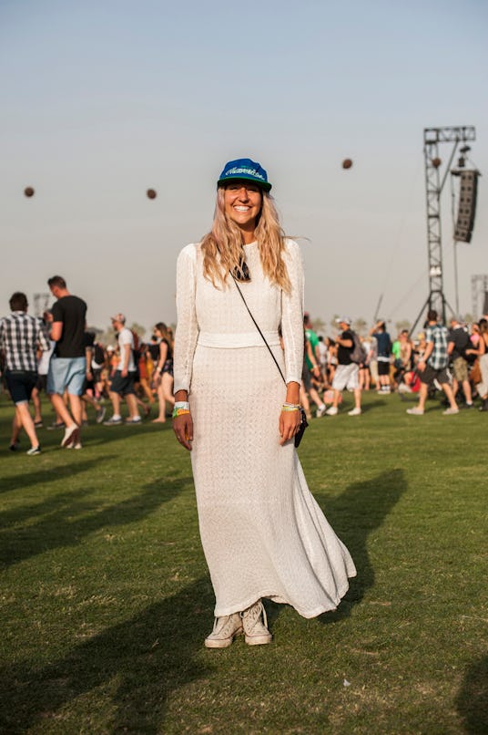 A woman in a long-sleeved light knit maxi dress, a blue cap and off-white Converse sneakers