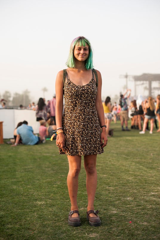 A woman with green hair, a short brown-beige dotted dress and brown shoes