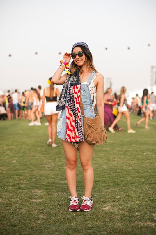 A woman in a white bralette, blue denim rompers, a long blue-red-white American flag print bandana a...