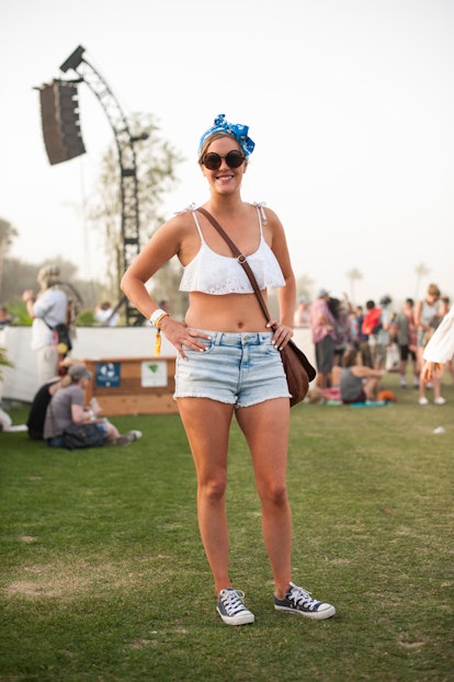 A woman in a white bralette, blue denim shorts, black and white Converse sneakers, blue headband and...