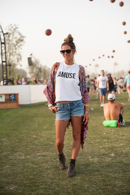 A woman in a white shirt with the words 'A muse', blue denim shorts, Aztec print kimono, black sungl...