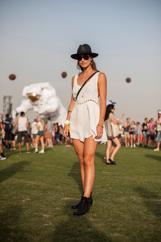 A woman in a short white dress black hat, black sunglasses and black ankle boots