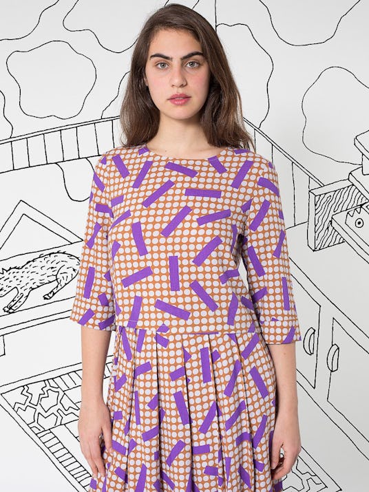 A model in a purple patterned dress standing in front of an illustrated mural