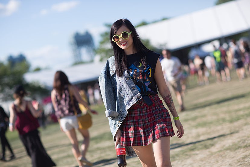 A woman at Governors Ball in a black top, plaid skirt and denim jacket over one shoulder 