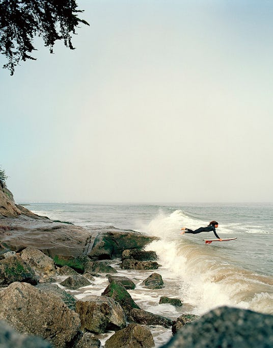 A person surfing on a wave next to beach rocks