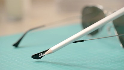 Ray-Ban sunglasses lying on a blue surface with a white pen pointing to an engraving "On"
