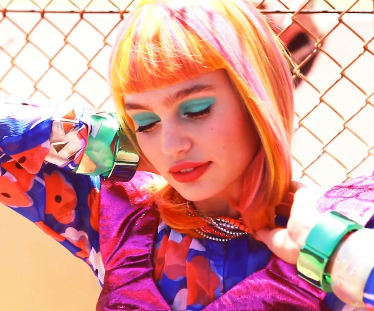 A model in a colorful outfit and orange and pink hair, turquoise eyeshadow and peach lipstick.