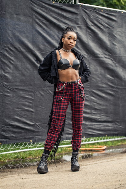 A girl wearing a black cropped denim jacket, black leather bra and red checkered pants with black le...