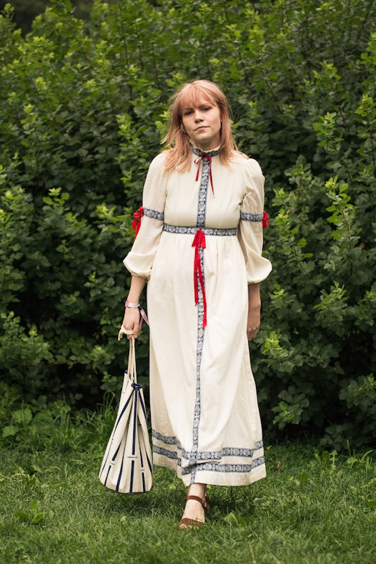 A girl with light pink hair in a white prairie dress with red ribbons on the collar, waist  and slee...