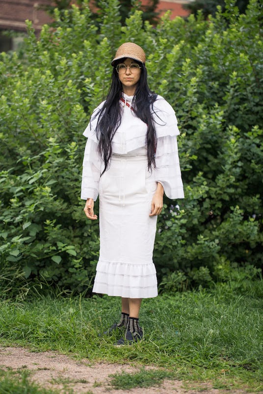 A black-haired woman wearing a white long-sleeved blouse and skirt, both with ruffles and a straw ca...