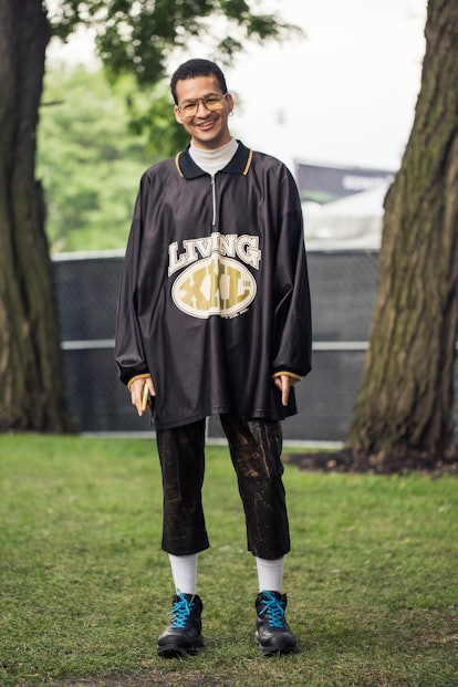 A man wearing an oversized jersey-type silk black collared shirt with long sleeves, that says "Livin...