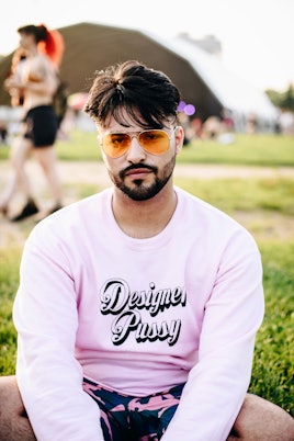 A man in a pink sweatshirt and orange sunglasses, sitting on the grass at Governor's Ball