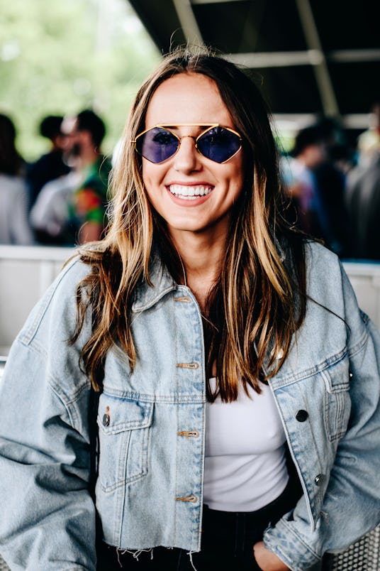 A woman laughing at Governor's Ball in a denim jacket, white tank top and diamond-shaped sunglasses 
