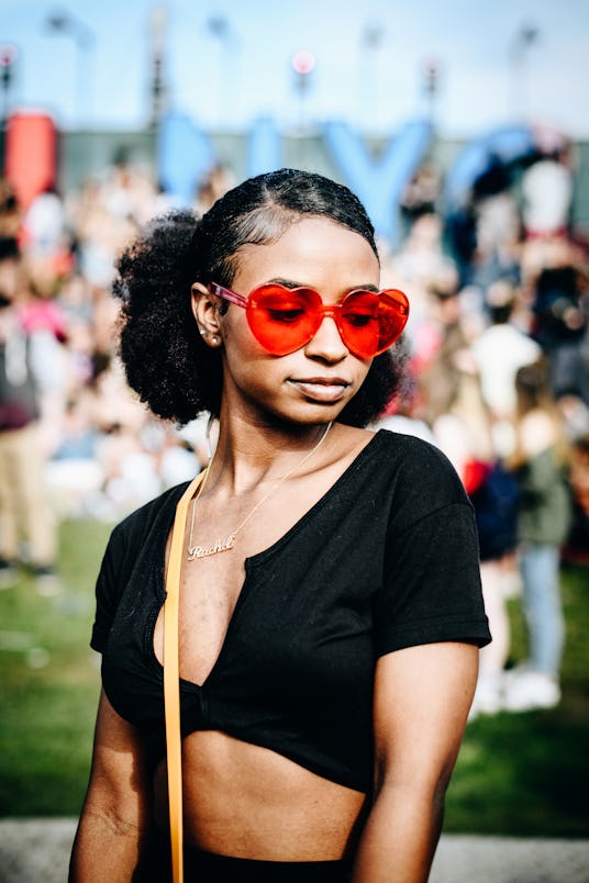 A woman in a black crop top, her hair slicked back and red heart-shaped sunglasses, posing at Govern...