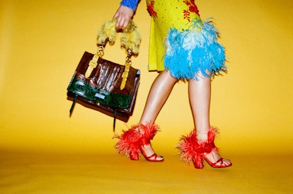 Brooke Smith wearing Prada, red heels, yellow skirt and green and brown handbag in front of yellow b...