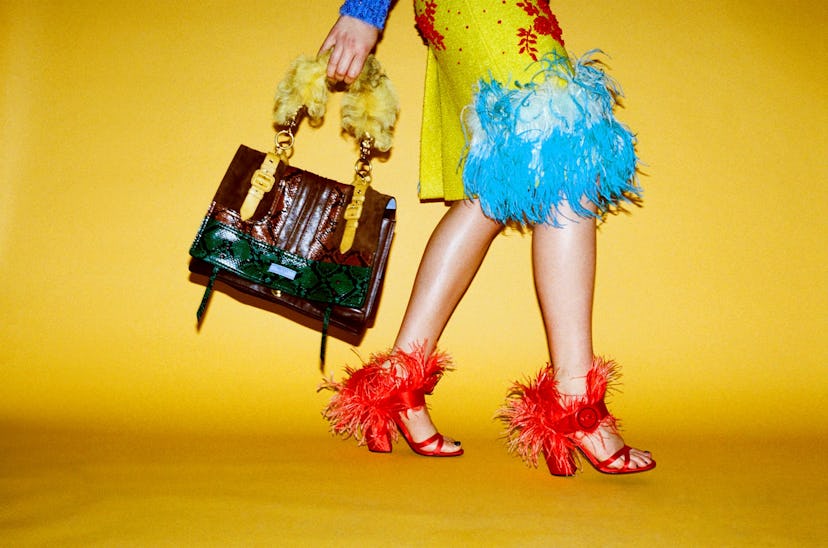 Brooke Smith wearing Prada, red heels, yellow skirt and green and brown handbag in front of yellow b...