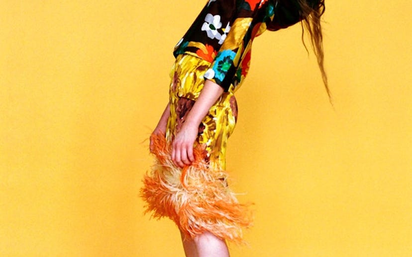 Brooke Smith in fancy outfit with green heels standing in front of the yellow background