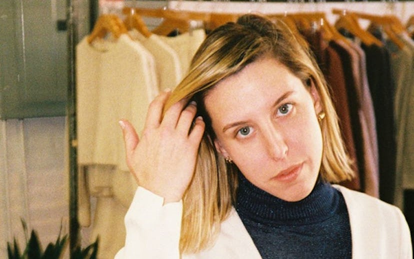Nikki Chasin brushing the hair from her face standing in front of a rack of her clothing designs