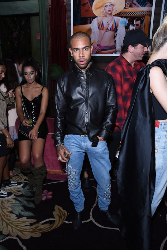 Vic Mensa posing in a leather shirt and blue jeans at Lauren Jauregui's party 