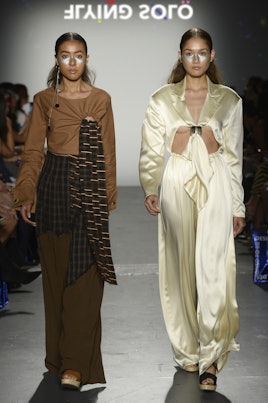 Two models in the Flying Solo show wearing Cemre Oktay: a brown dress with dark brown detailing and ...