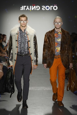 Two models in the Flying Solo show in Acid NY: a faux fur jacket and grey pants, and orange pants wi...