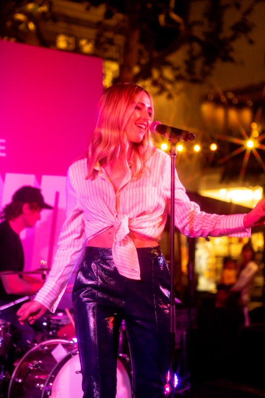 Katelyn Tarver on the stage with a microphone in front of her wearing a white tied crop top a black ...