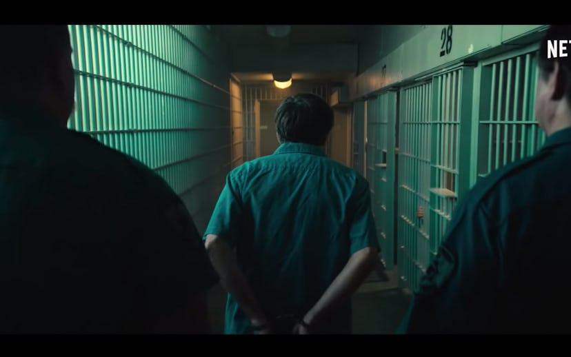 Two police officers walking by cells with a man in front of them with handcuffs in jail