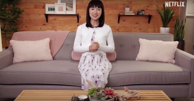 Marie Kondo sitting on a couch in a scene from her "Tidying Up".
