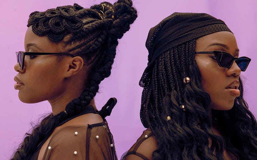 VanJess posing back to back, both wearing sunglasses and sheer black blouses
