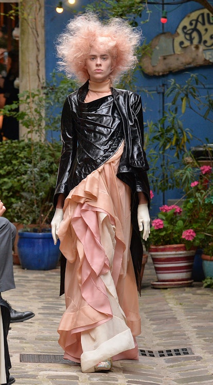 A model walking a runway, wearing a long black jacket with ruffles and a poofy skirt that has layers...