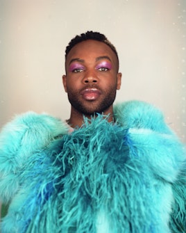 Todrick Hall posing in a turquoise faux fur coat while wearing purple eyeshadow 