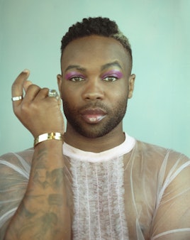 Todrick Hall posing in a white tulle blouse with ruffles in the middle  