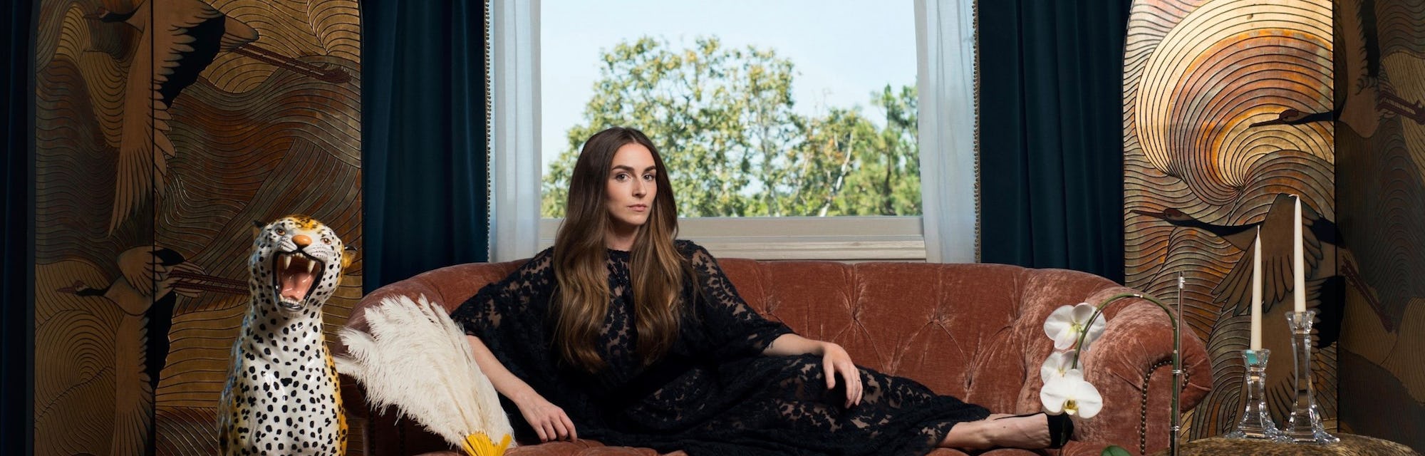 Annamarie Tendler Mulaney posing on a couch while wearing a long black dress