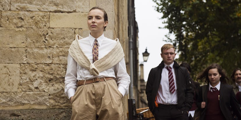 Jodie Comer wearing a white button-up, a tie, tan trousers, and a sweater wrapped around her shoulde...