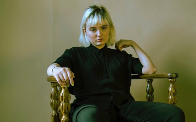 Jackie Carlson, star of 'Family Reunion,' in a black shirt and green pants, sitting on an antique ch...