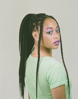 Salem Mitchell with her hair up, in a green t-shirt and blue and purple eye makeup, with purple lips...