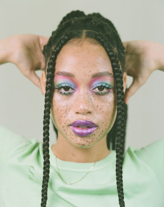 Salem Mitchell with her hair up, in a green t-shirt and blue and purple eye makeup, with purple lips...
