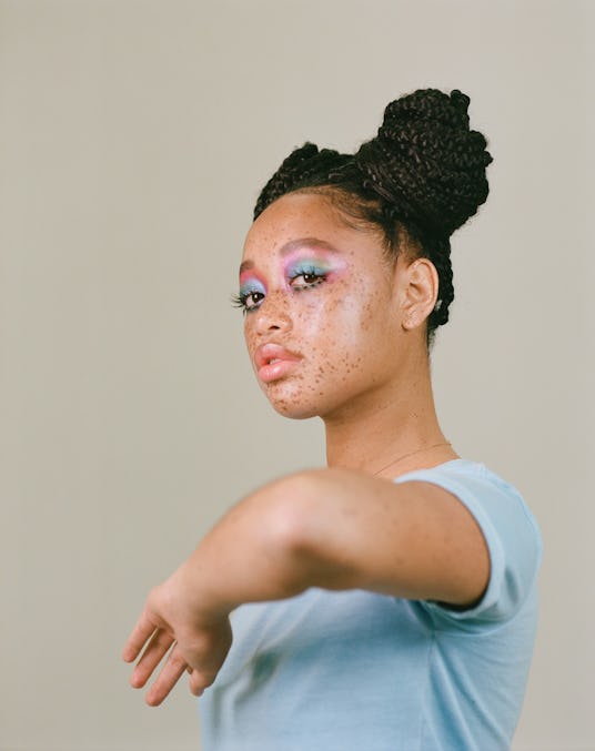 Salem Mitchell with her hair up in space buns, in a blue t-shirt, and blue and purple eye makeup, wi...