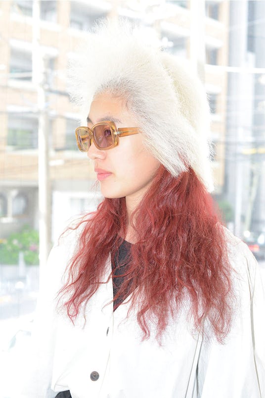 A woman in orange glasses with red hair under a ash blonde wig for Tomi Kono's "Personas" Exhibition