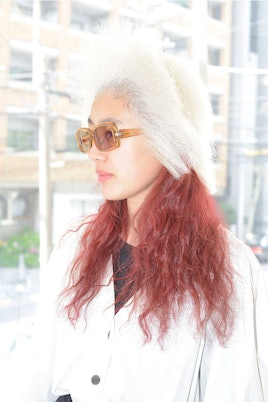 A woman in orange glasses with red hair under a ash blonde wig for Tomi Kono's "Personas" Exhibition