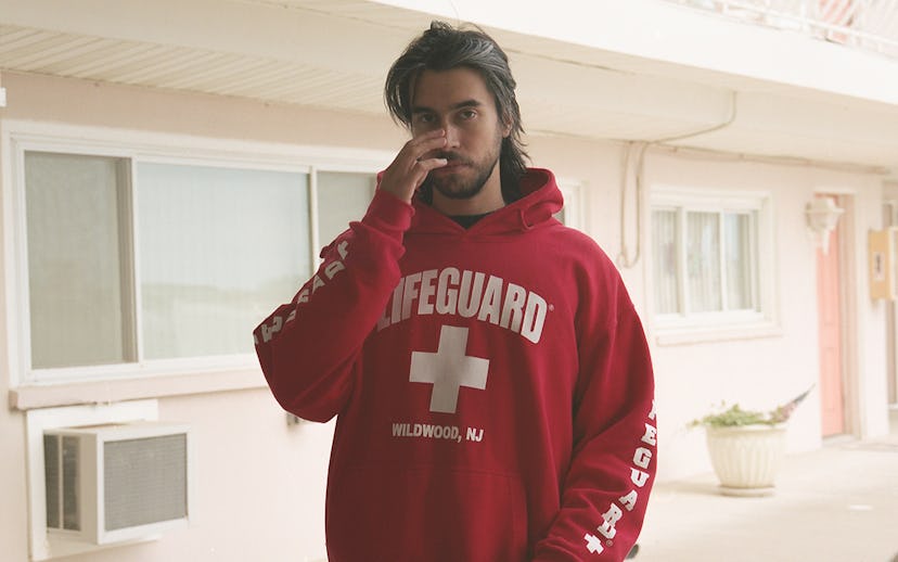 Long-haired Alex G wearing a red hoodie with "lifeguard" text on it