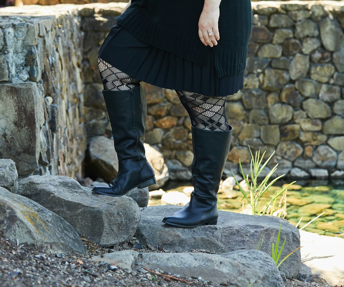 A woman wearing calf-length black boots paired with a black dress