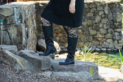 Close-up woman wearing calf-length black boots paired with a black dress.
