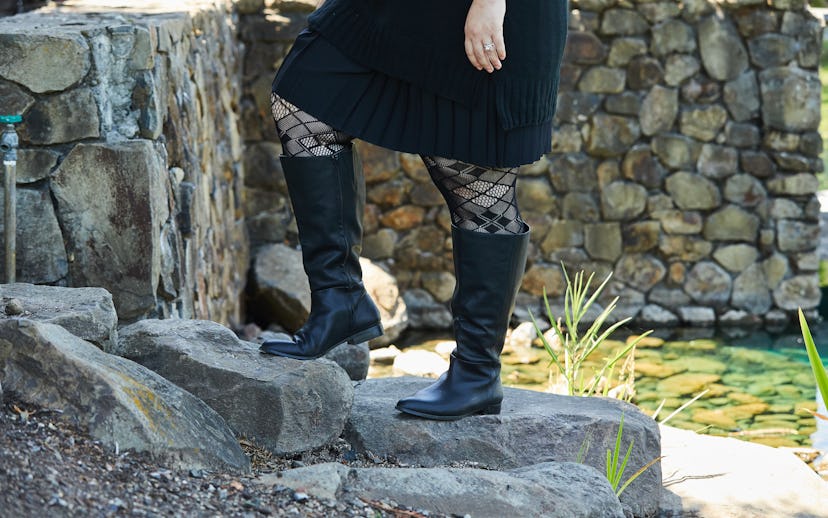 A woman wearing calf-length black boots paired with a black dress