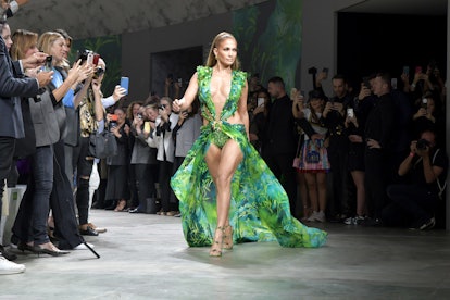 Jeniffer Lopez posing and looking to the side in a sleeveless green Versace gown with a palm tree pr...