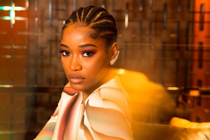 Keke Palmer  with tightly braided hair and in a pink shirt looking at the camera in front of a patte...